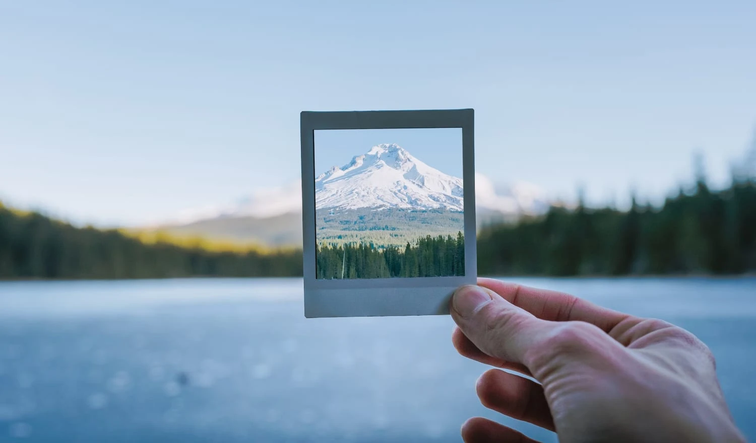 A man holding a polaroid of a snowy mountain