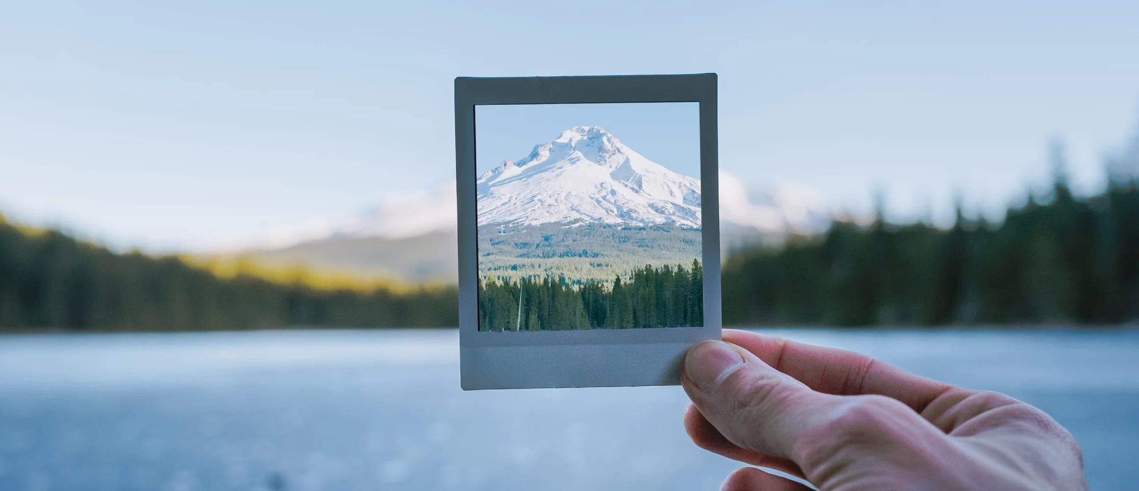 A man holding a polaroid of a snowy mountain