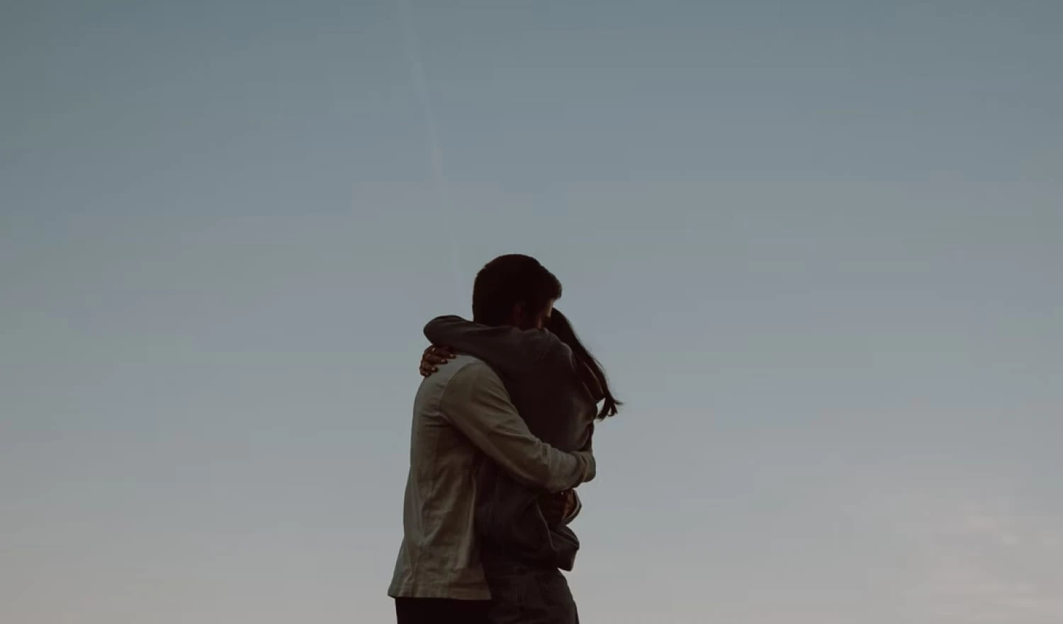 A couple hugging in front of a blue sky