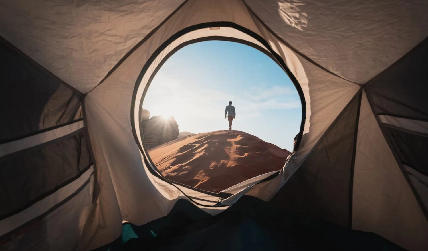 A man walking out of a tent and into sand dunes