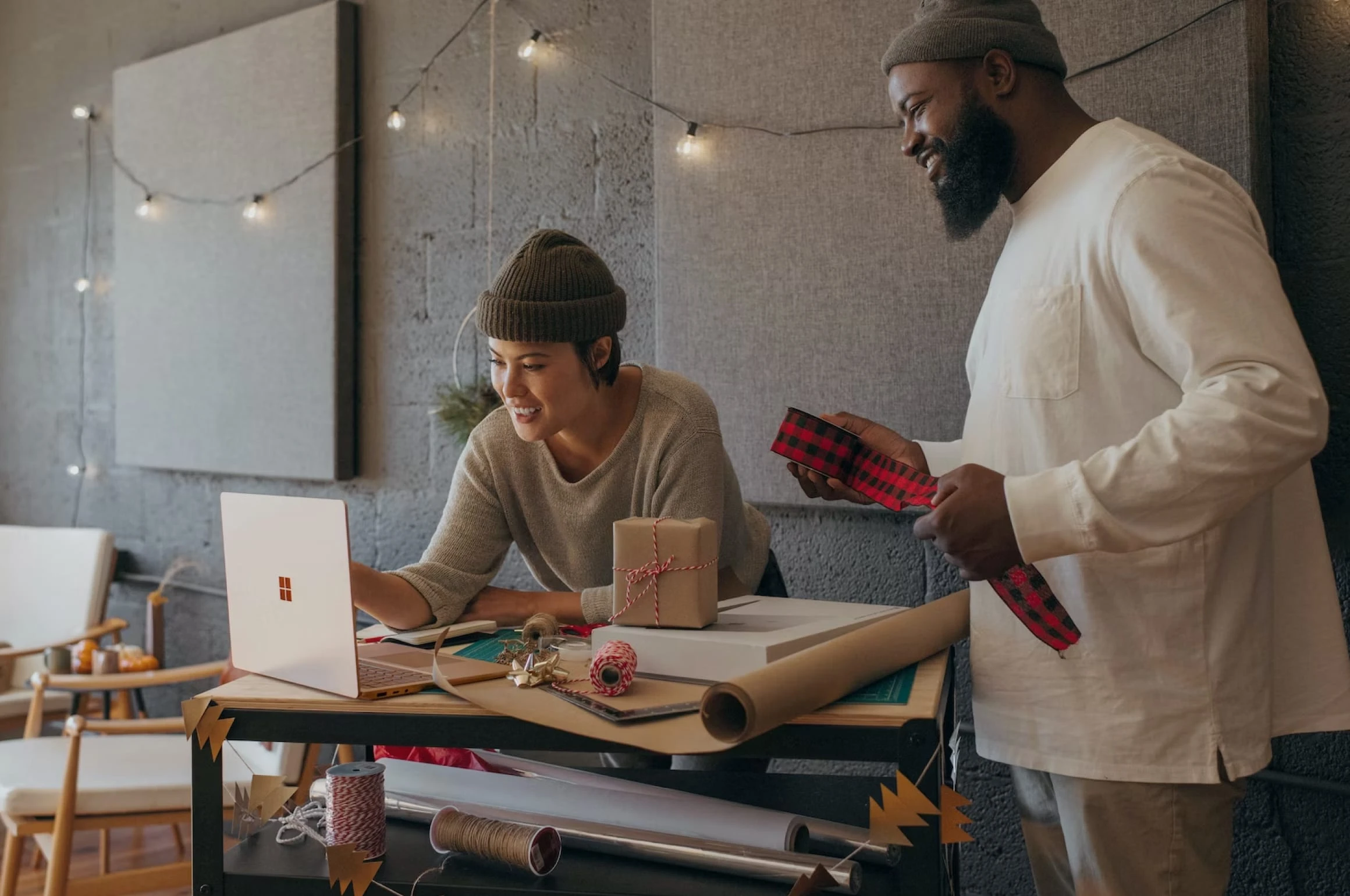 A couple unwrapping presents in the office while looking at a laptop