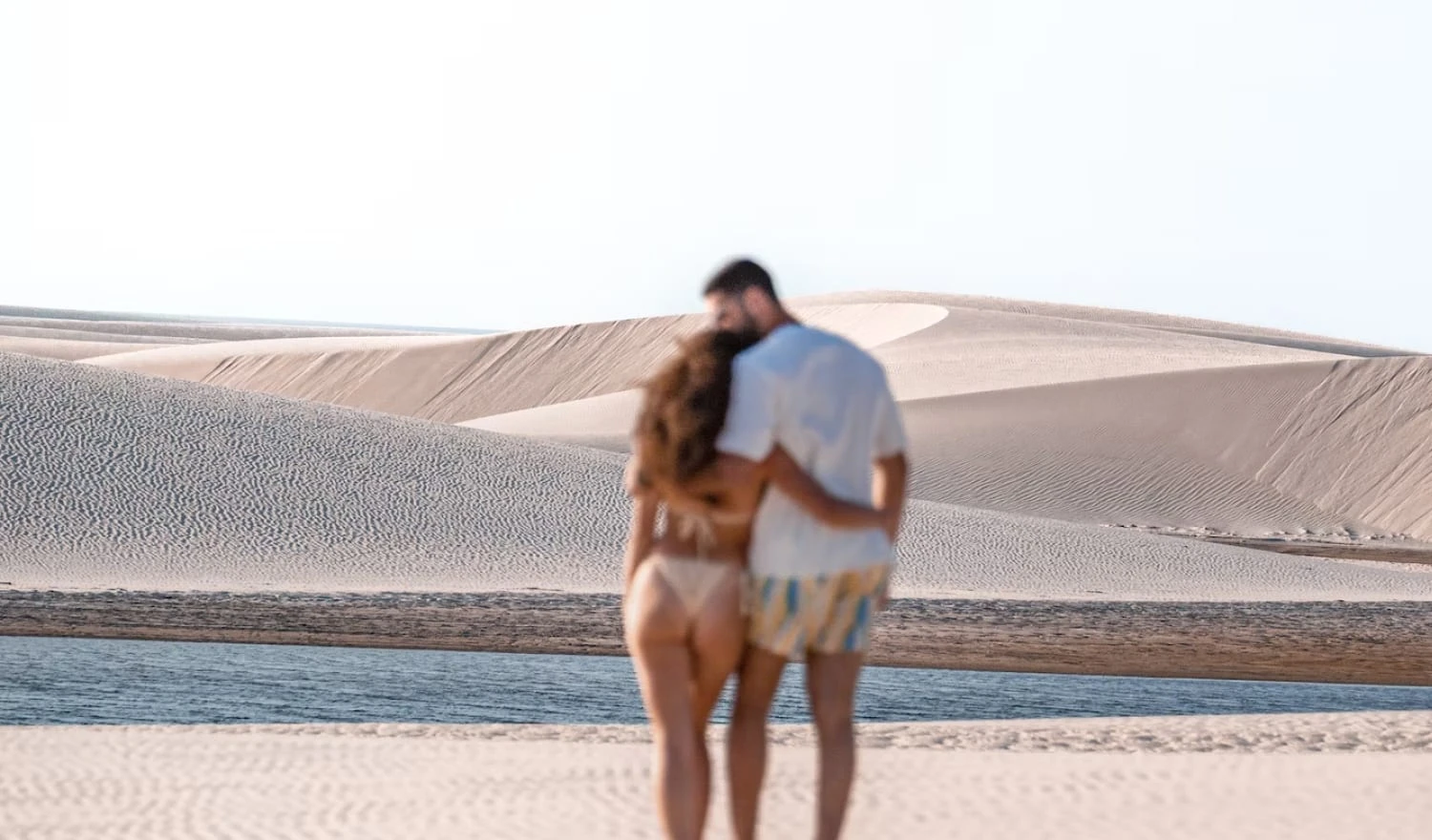 A couple in swimsuits walking on a bright beach.