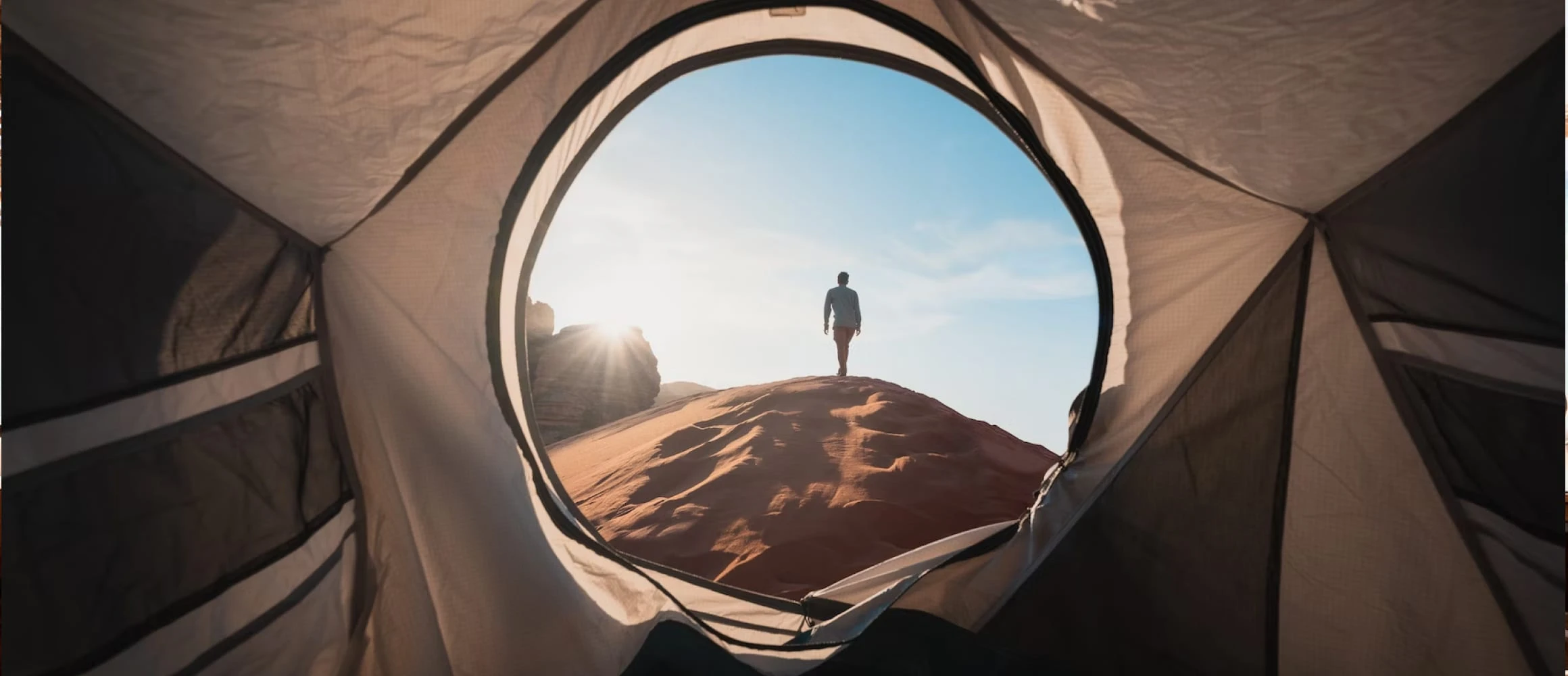 A man walking out of a tent and into sand dunes