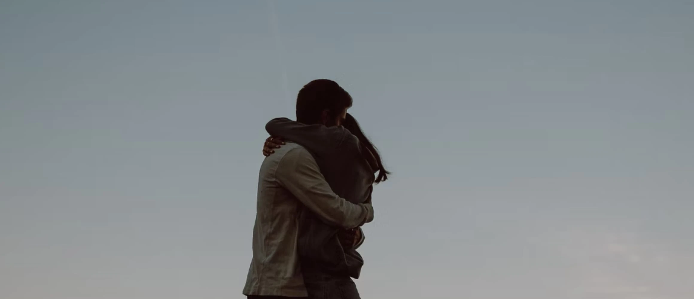 A couple hugging in front of a blue sky